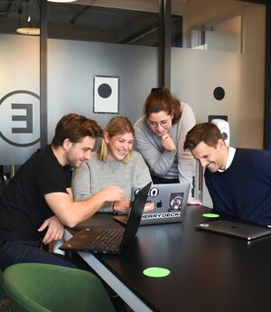 Vier collega's overleggen lachend rond twee laptops aan een vergadertafel